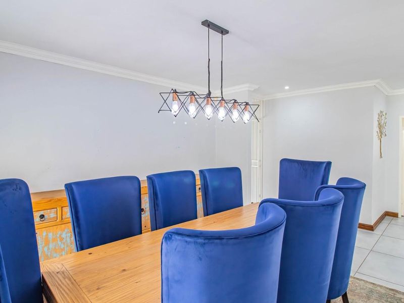 A bright dining room featuring tiled flooring, crown molding, and a contemporary pendant light fixture, with a view into an adjacent bathroom.
