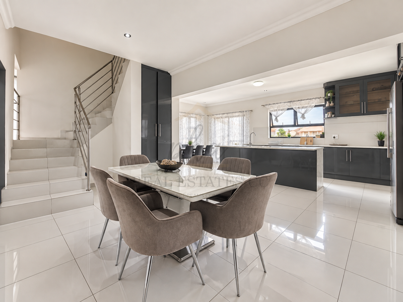 Modern open-plan living and dining area featuring sleek kitchen cabinetry, a central island, and a contemporary staircase with a metal balustrade.