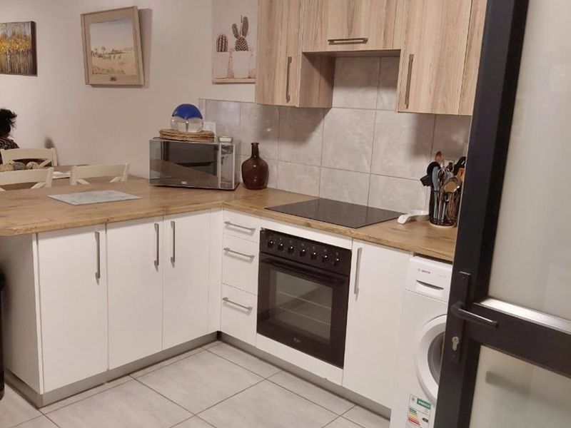 A functional kitchen featuring white base cabinets, wood-look upper cabinets, laminate countertops, tiled backsplash, and integrated appliances including an oven, hob, and washing machine.