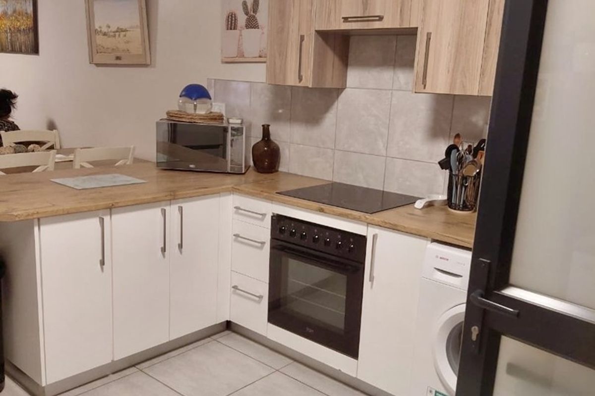 A functional kitchen featuring white base cabinets, wood-look upper cabinets, laminate countertops, tiled backsplash, and integrated appliances including an oven, hob, and washing machine.