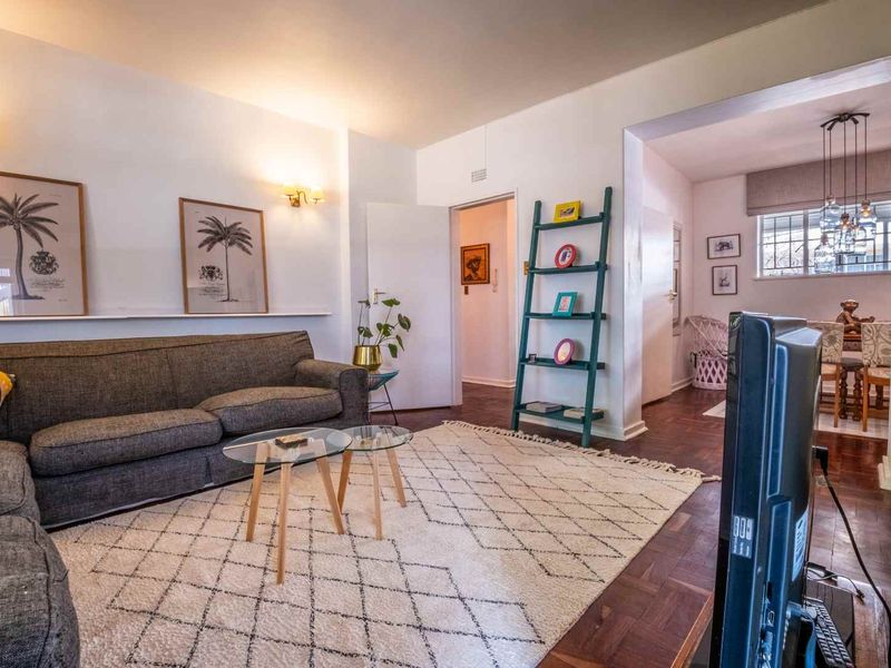 A well-maintained living room featuring classic parquet flooring, wall-mounted lighting, and a built-in display ledge, flowing into an adjacent dining area.