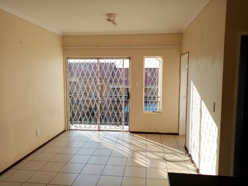 An empty living room featuring tiled flooring, a sliding security gate leading to a balcony, and security bars on the window.