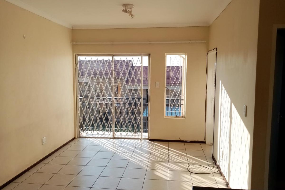 An empty living room featuring tiled flooring, a sliding security gate leading to a balcony, and security bars on the window.