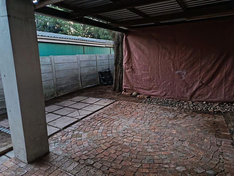A covered outdoor patio area featuring circular brick paving and a concrete support pillar, enclosed by a precast concrete boundary wall.