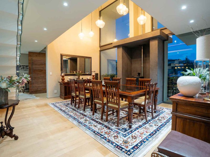 Elegant dining room featuring double-volume ceilings, large windows, hardwood flooring, and a central fireplace, creating a sophisticated and airy atmosphere.