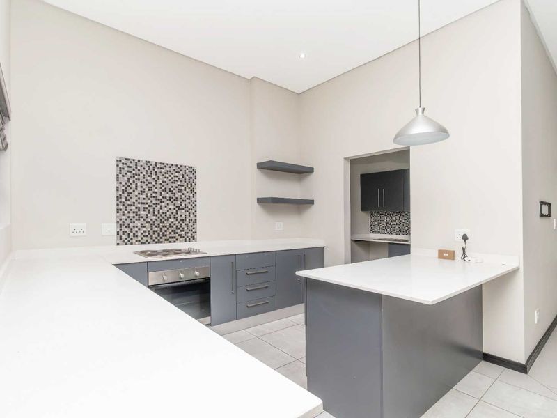 Modern kitchen featuring grey cabinetry, stone countertops, a gas hob, built-in oven, and a functional island, with an adjacent scullery area.