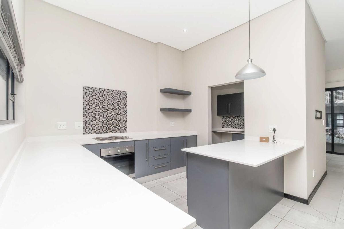 Modern kitchen featuring grey cabinetry, stone countertops, a gas hob, built-in oven, and a functional island, with an adjacent scullery area.