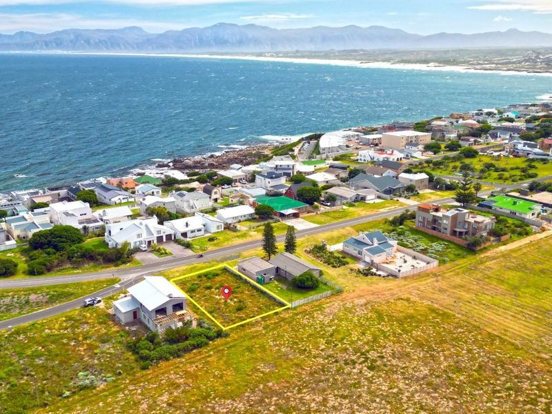 Aerial view of a vacant residential plot situated in a coastal neighborhood with scenic ocean and mountain views.