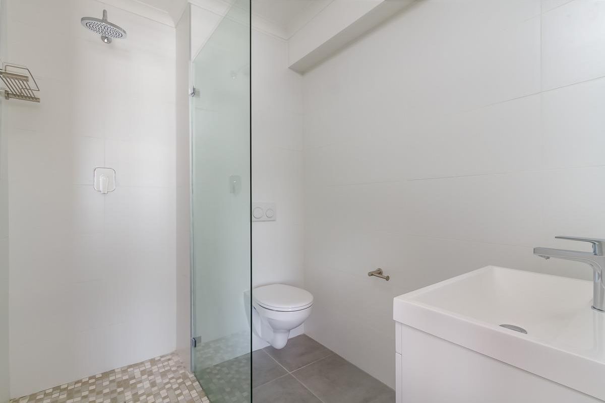 Modern bathroom featuring a walk-in shower with a glass screen, wall-mounted toilet, and a sleek vanity basin with chrome fixtures.