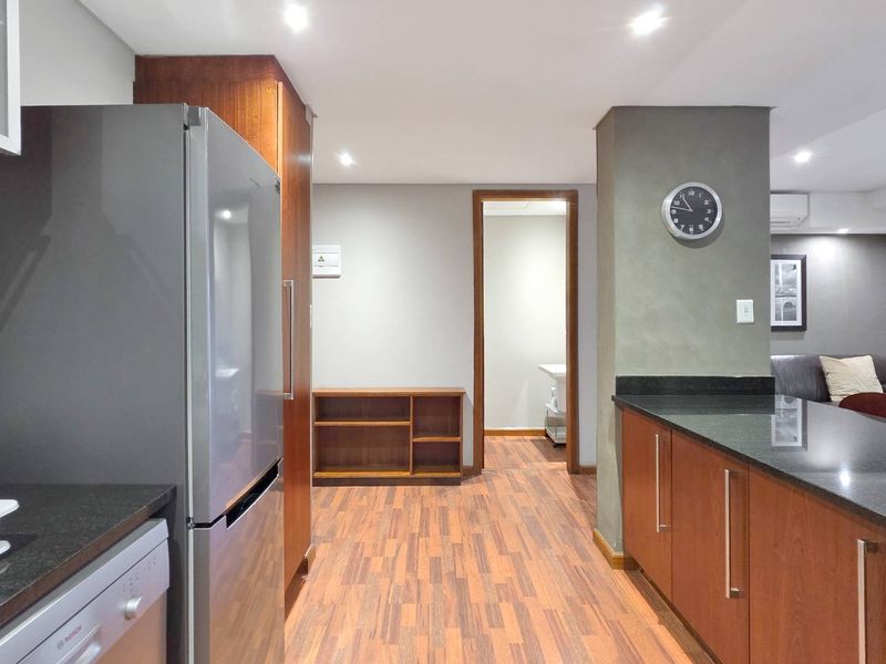 A well-maintained kitchen featuring warm wood-toned cabinetry, dark granite countertops, and modern recessed lighting, seamlessly flowing into the adjacent living area.