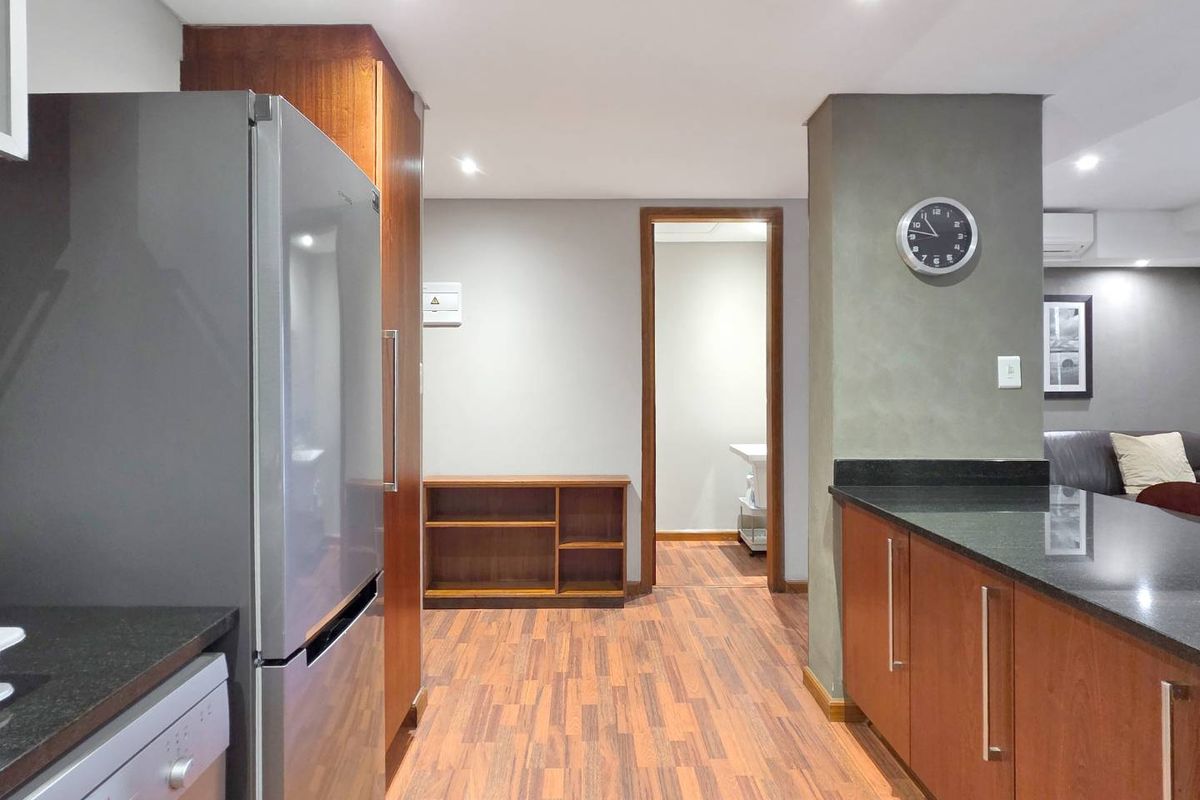 A well-maintained kitchen featuring warm wood-toned cabinetry, dark granite countertops, and modern recessed lighting, seamlessly flowing into the adjacent living area.