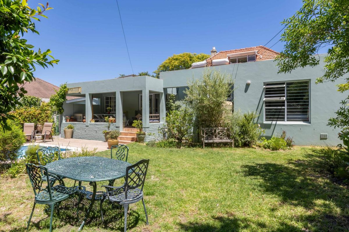 Rear view of the property featuring a covered patio, swimming pool, and a landscaped garden area with established greenery.