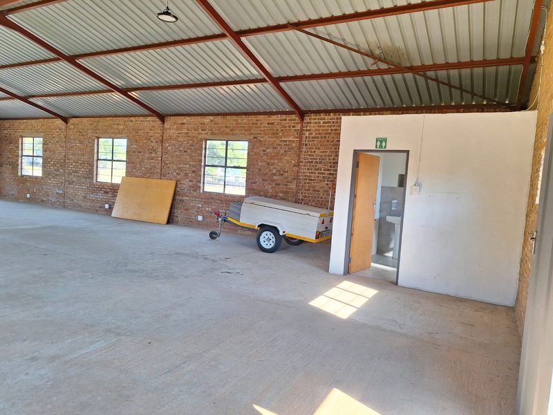 Spacious industrial utility area featuring exposed brick walls, concrete flooring, and a high-pitched corrugated metal roof with an integrated restroom facility.