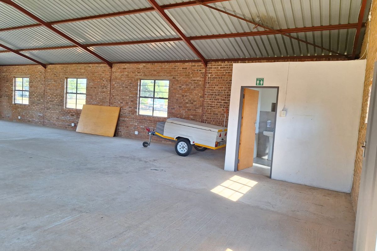 Spacious industrial utility area featuring exposed brick walls, concrete flooring, and a high-pitched corrugated metal roof with an integrated restroom facility.