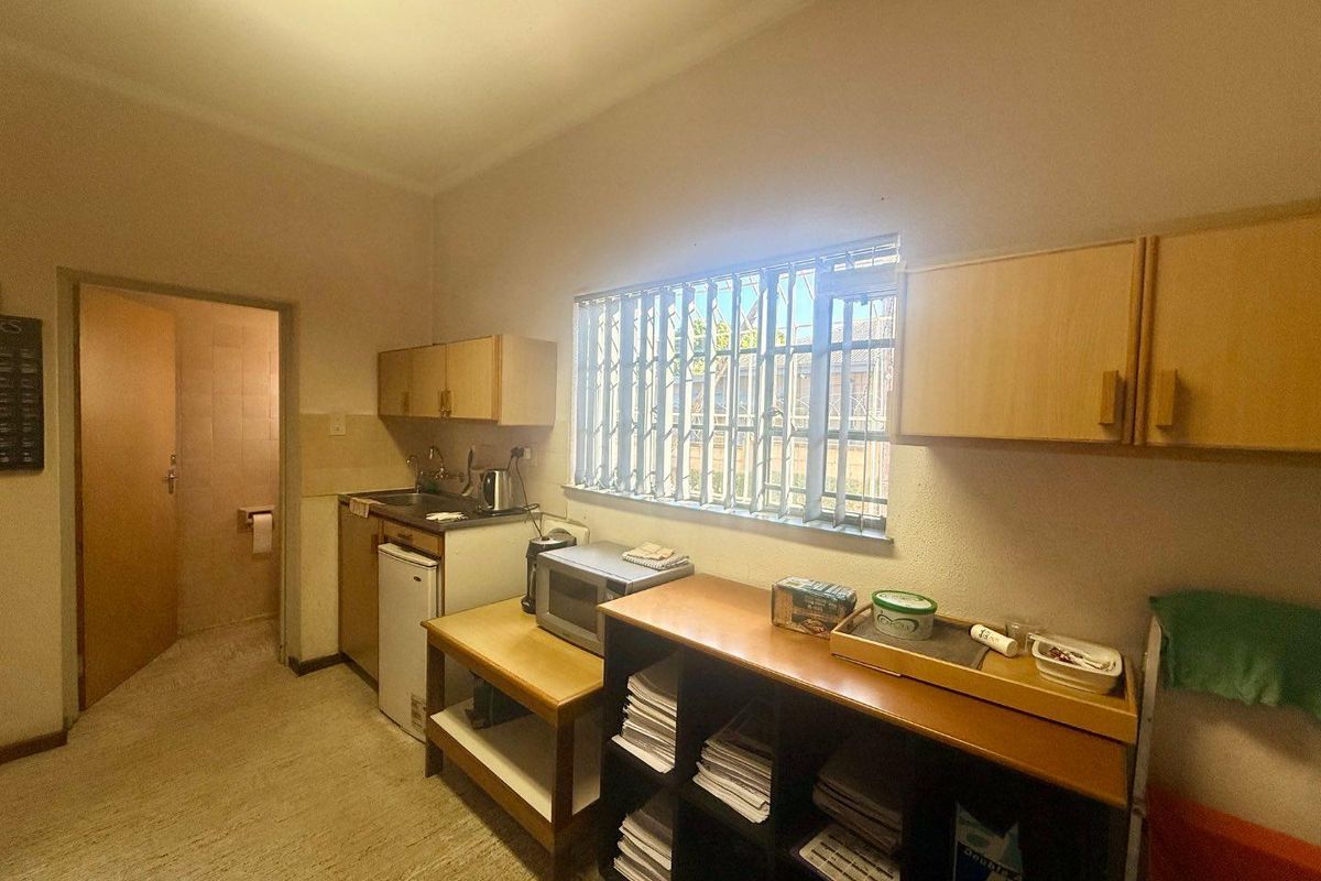 A functional office kitchenette featuring built-in cabinetry, a sink, and a window with security bars, providing a practical break area for staff.