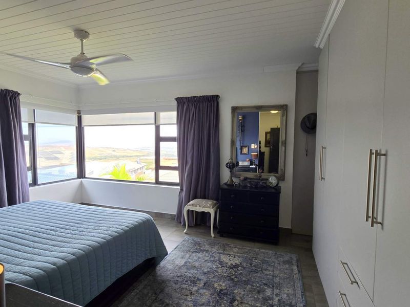 Spacious bedroom featuring built-in cupboards, a ceiling fan, and large windows offering expansive views.