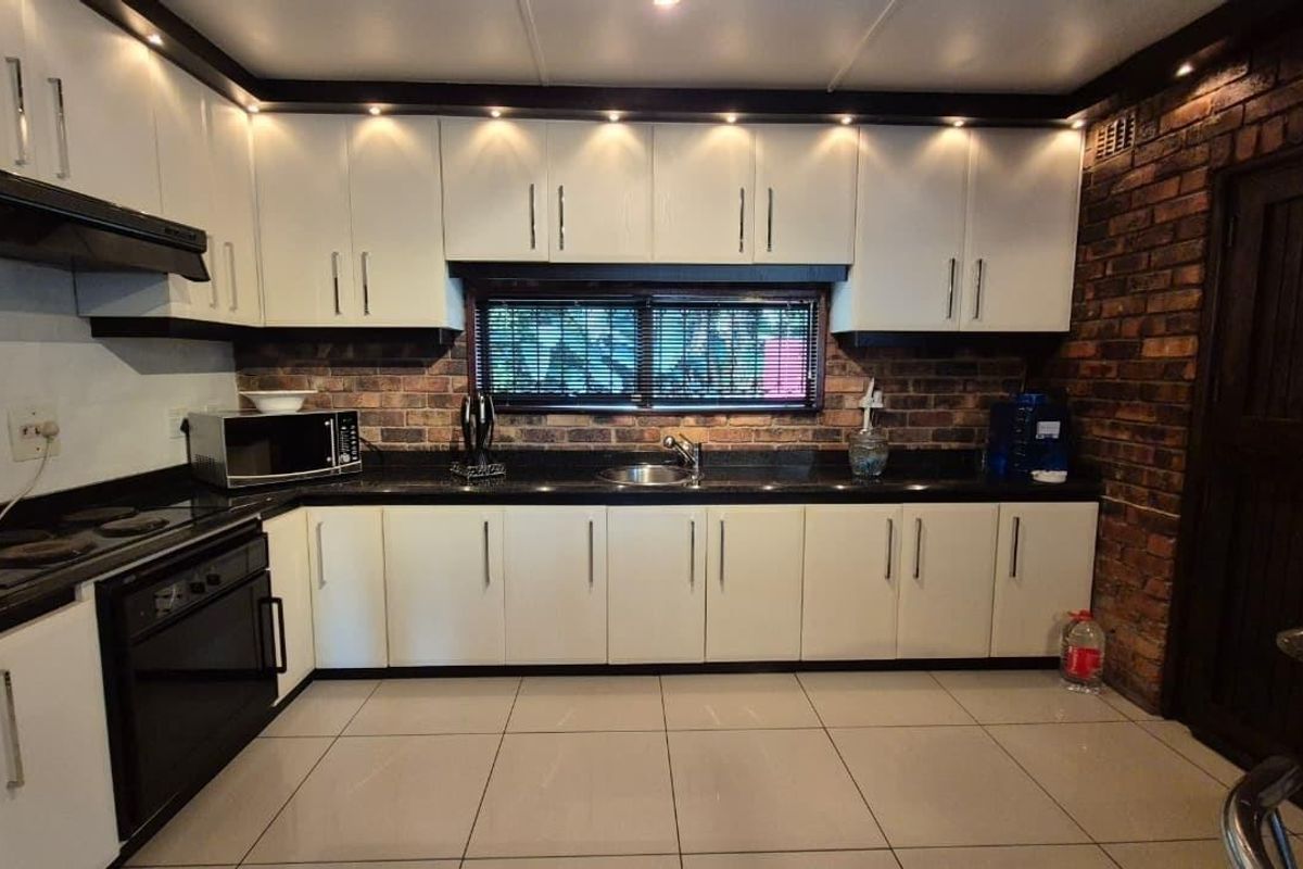 A well-maintained kitchen featuring white cabinetry, black granite countertops, an exposed brick wall, and integrated appliances with modern recessed lighting.
