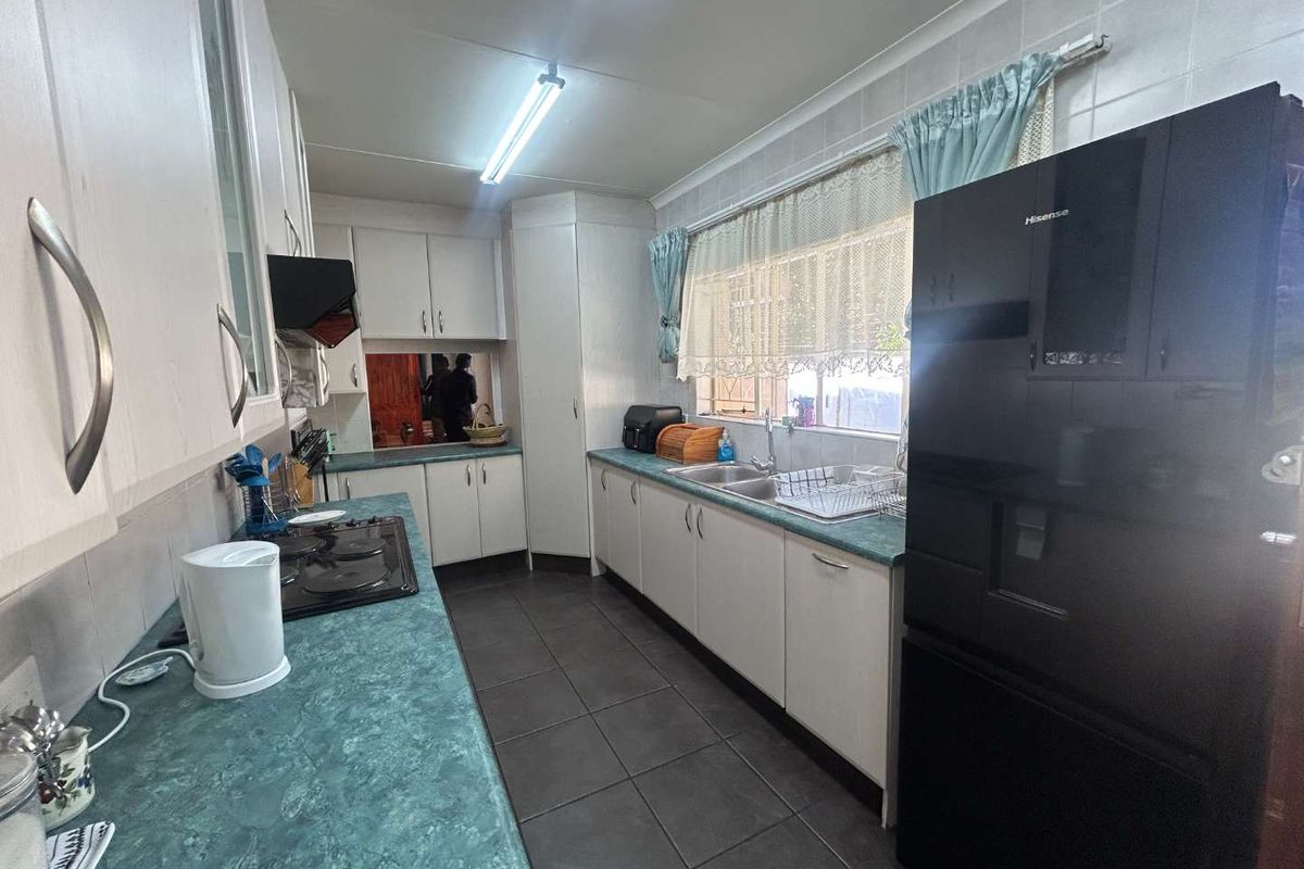 Functional kitchen featuring laminate countertops, ample built-in cabinetry, a double bowl sink, and tiled flooring with a tiled splashback.