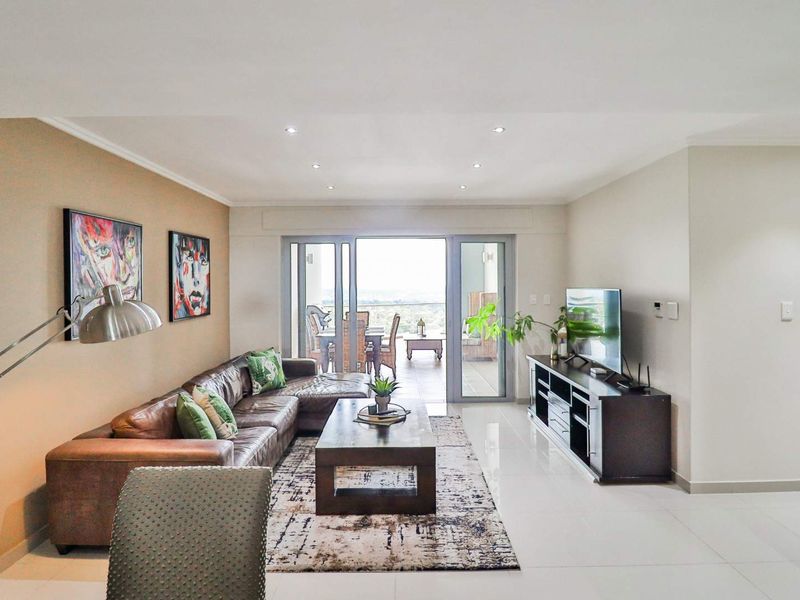 A bright and modern living room featuring tiled floors, recessed lighting, and large sliding glass doors that open onto an outdoor patio area.