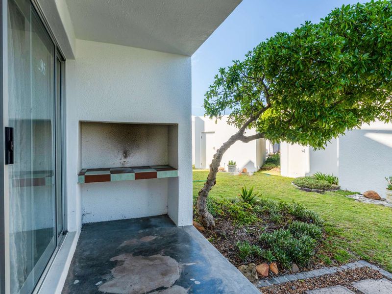Covered patio area featuring a built-in braai, concrete flooring, and direct access to a private garden space through sliding glass doors.