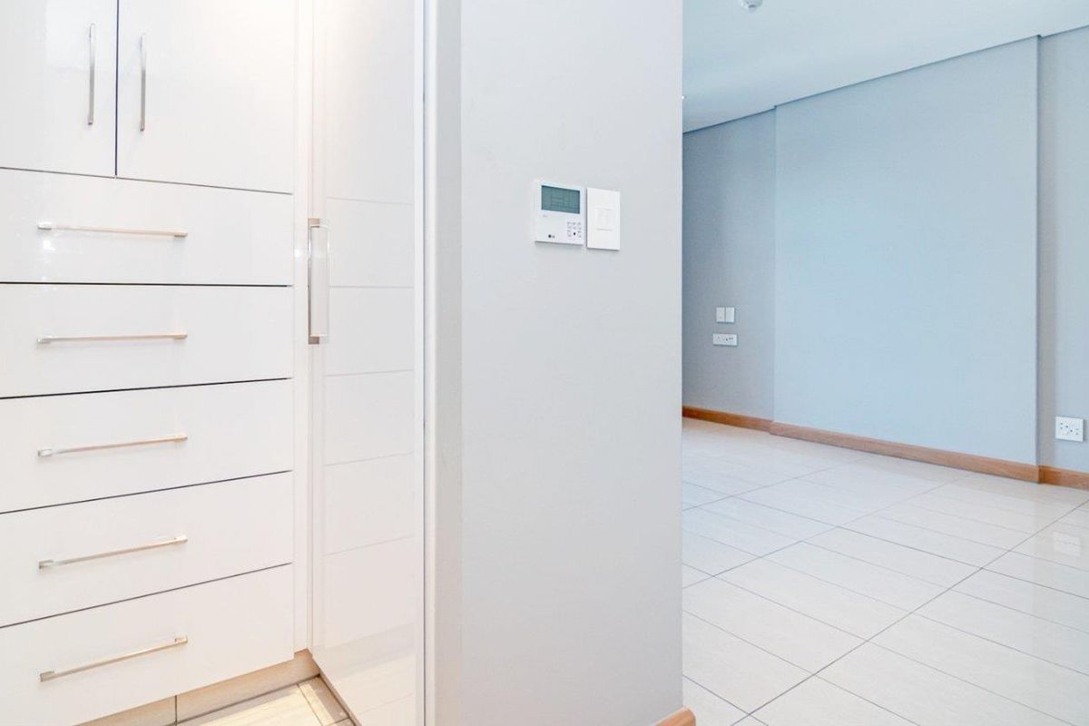 A bright, modern interior space featuring high-gloss white built-in cabinetry, tiled flooring, and a wall-mounted climate control unit.