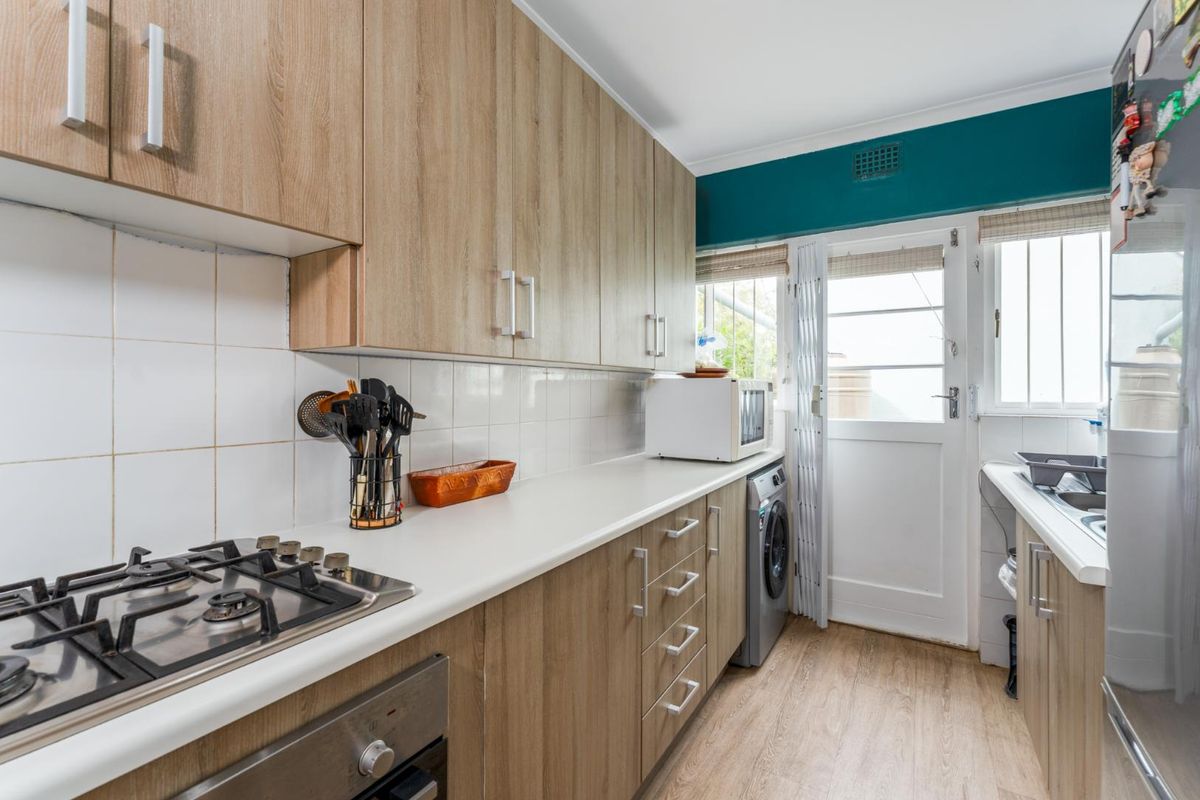 A functional kitchen featuring light wood-look cabinetry, a built-in gas hob, oven, and integrated laundry space with direct access to the exterior.