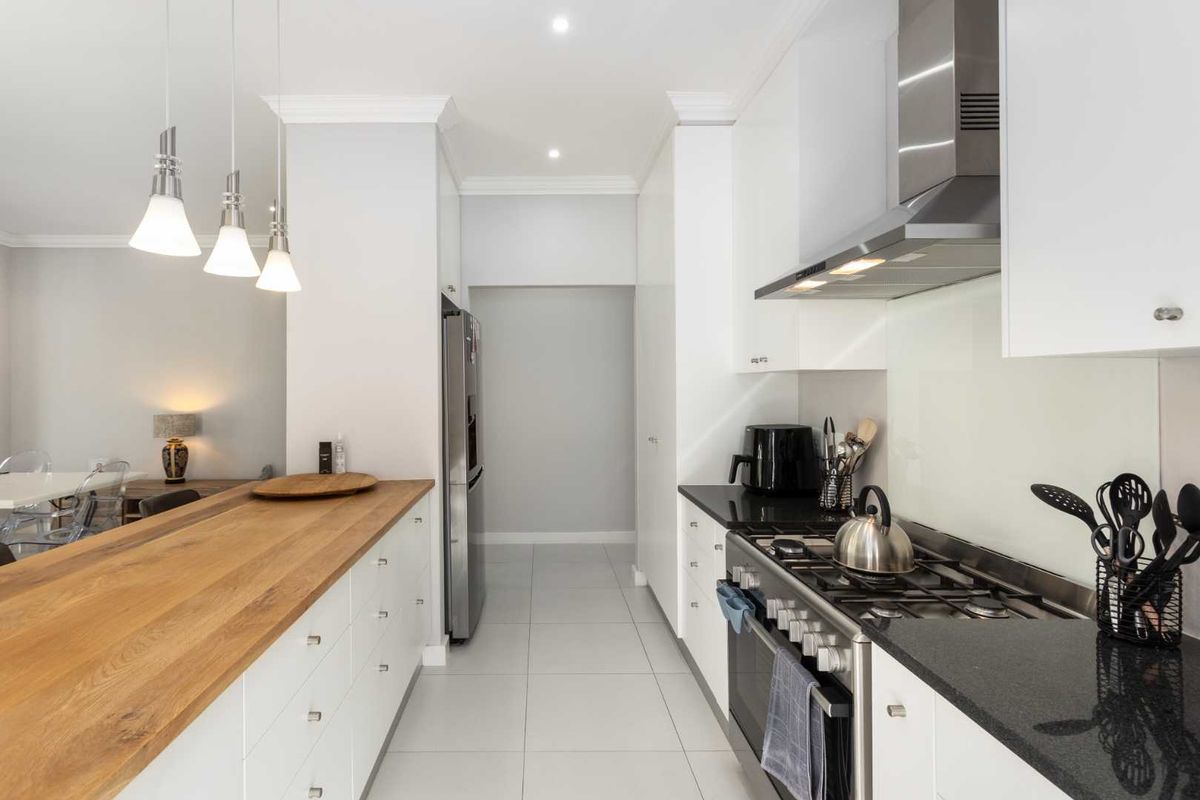 Modern kitchen featuring white cabinetry, black granite countertops, a wooden breakfast bar, stainless steel gas stove, and integrated extractor fan.