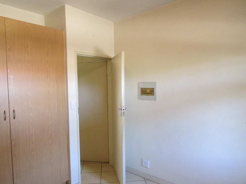 A clean, empty bedroom featuring built-in wooden wardrobes, tiled flooring, and a wall-mounted electrical distribution board.