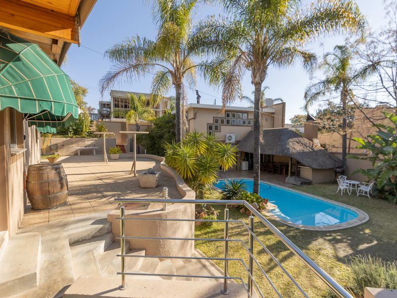 Rear exterior view featuring a swimming pool, a thatched lapa entertainment area, and a paved patio with stainless steel balustrades.