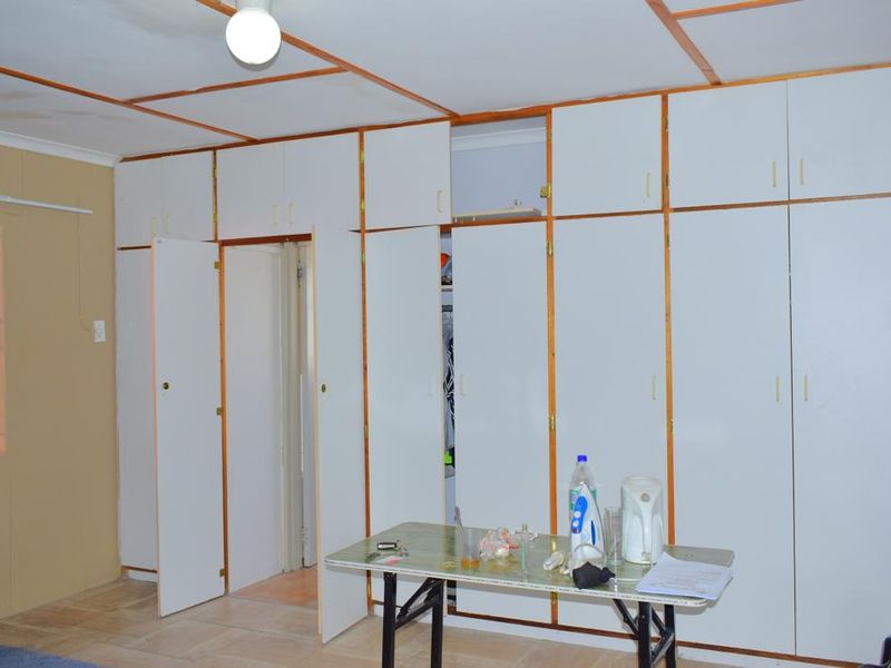 Bedroom featuring extensive built-in cupboard storage, tiled flooring, and security bars on the window. The room requires cosmetic updates to the cabinetry and ceiling.