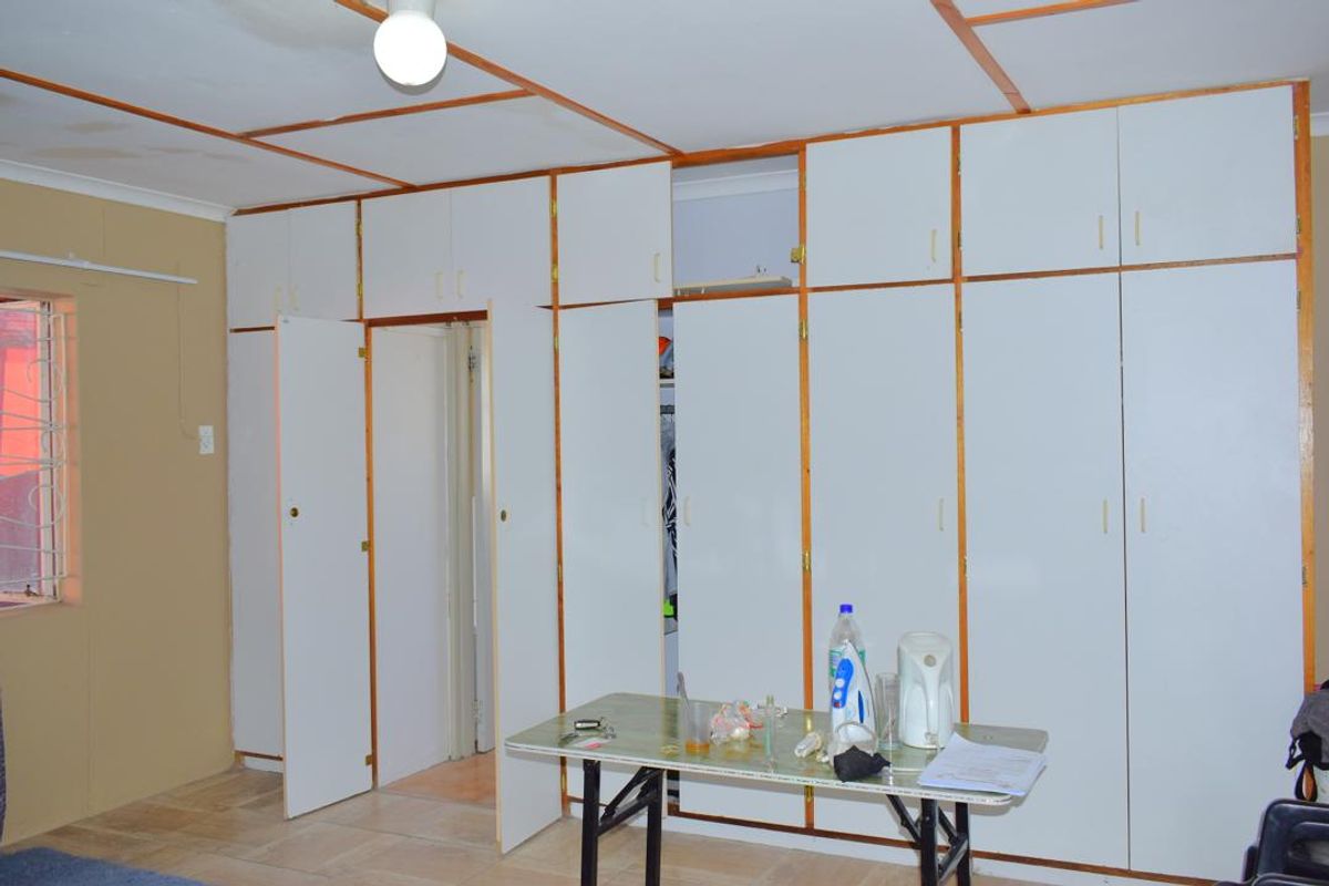 Bedroom featuring extensive built-in cupboard storage, tiled flooring, and security bars on the window. The room requires cosmetic updates to the cabinetry and ceiling.