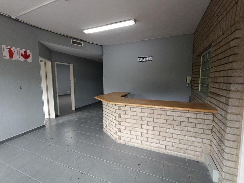 Industrial reception area featuring a built-in brick counter, ceramic tiled flooring, and neutral grey walls, providing a functional entry space for the property.