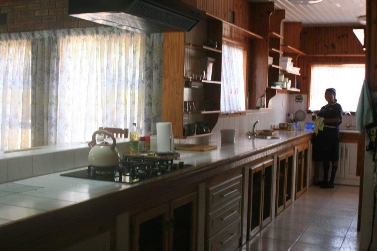 A dated kitchen featuring extensive timber cabinetry, tiled countertops, and integrated cooking appliances, offering a traditional layout with ample storage space.