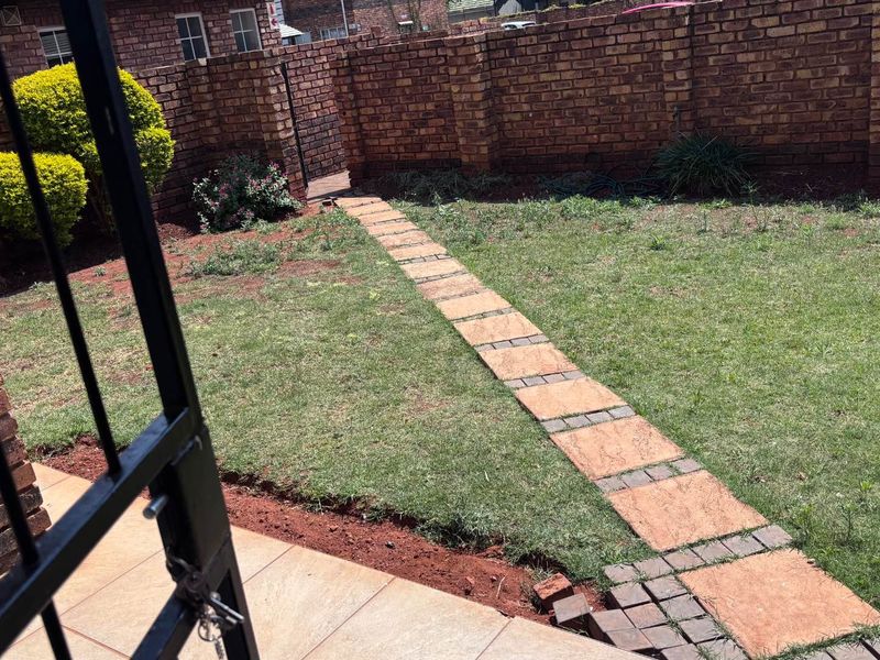 A private rear garden featuring a brick boundary wall, a lawn area, and a paved walkway leading through the yard.