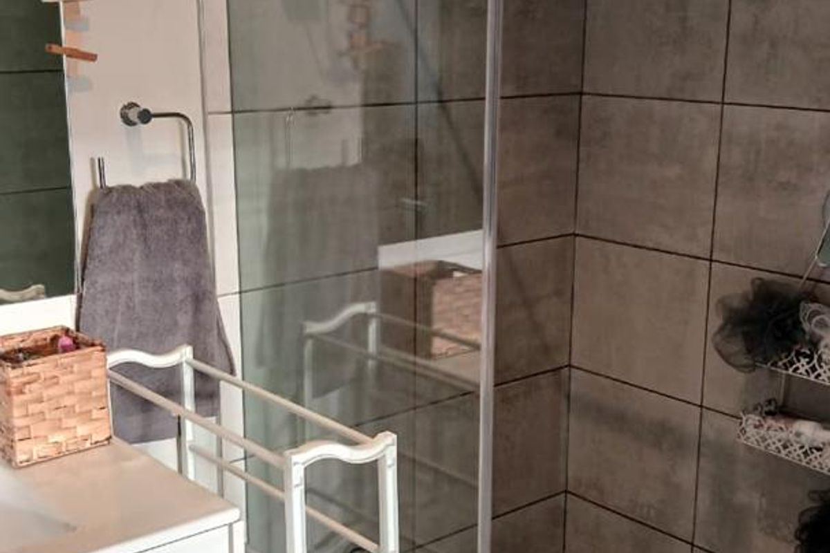 A modern bathroom featuring a glass-enclosed walk-in shower with grey tiled walls and a wall-mounted vanity unit.