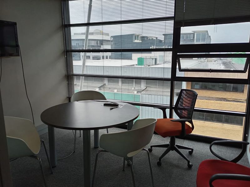 A functional office space featuring large floor-to-ceiling windows with venetian blinds, providing ample natural light and an urban view.