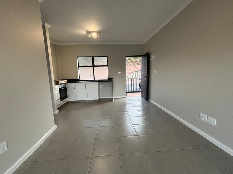 An open-plan living and kitchen area featuring neutral tiled floors, modern white cabinetry, built-in oven and hob, and direct access to an outdoor space.