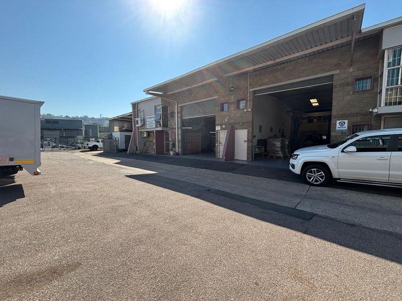 Industrial property exterior featuring large roller shutter doors, concrete yard space, and functional access points for commercial or warehouse operations.