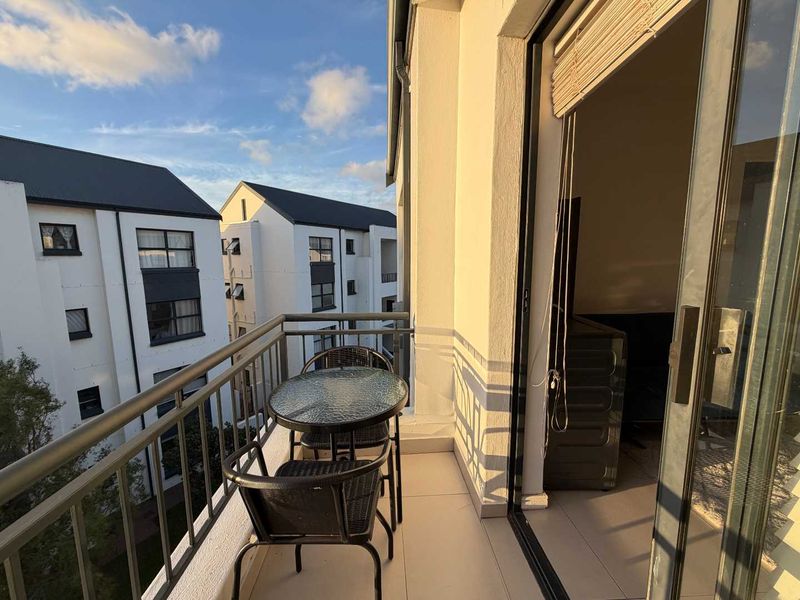 A private balcony featuring tiled flooring and a metal railing, providing an outdoor extension to the apartment living space.