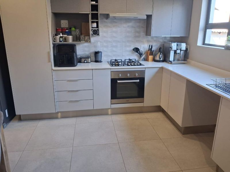 Modern kitchen featuring sleek grey cabinetry, stone countertops, a gas hob, and an integrated oven with a tiled backsplash and floor.