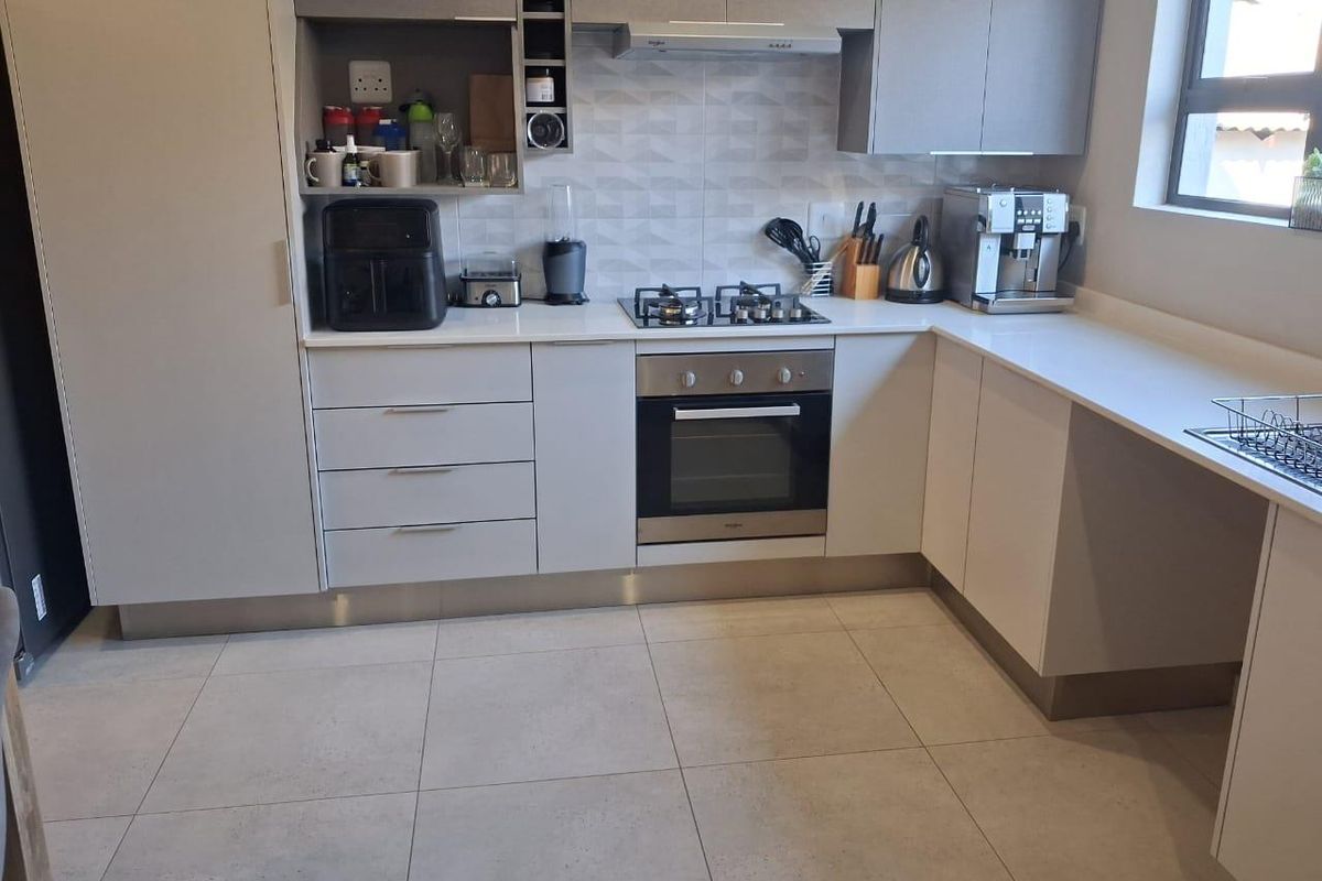 Modern kitchen featuring sleek grey cabinetry, stone countertops, a gas hob, and an integrated oven with a tiled backsplash and floor.