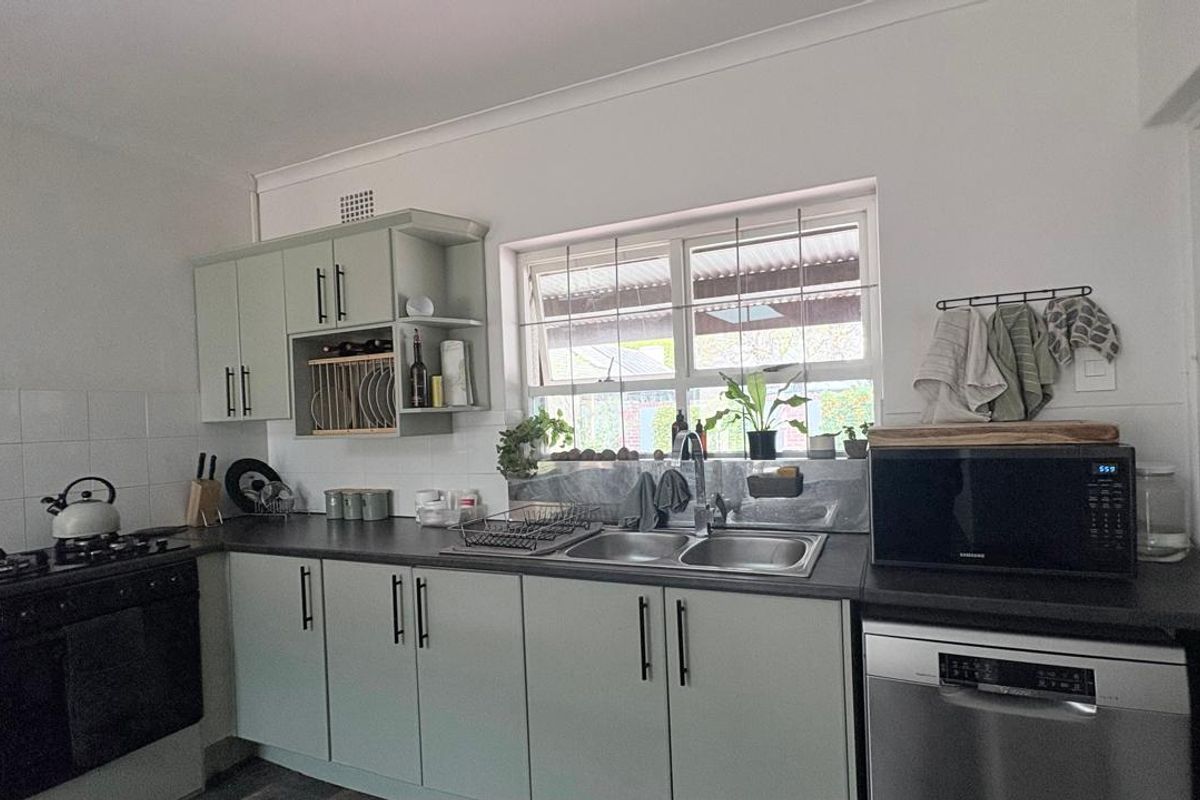 A functional kitchen featuring light green cabinetry, dark countertops, a stainless steel double sink, and a built-in gas hob and oven.