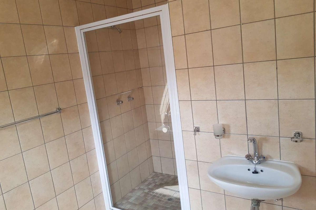 A functional bathroom featuring a walk-in shower with a white frame, wall-mounted basin, and neutral ceramic wall tiles.