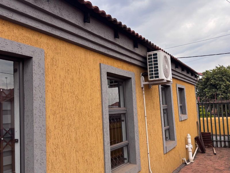 Rear exterior view of the property featuring textured yellow walls, grey trim, a mounted air conditioning unit, and a paved patio area.