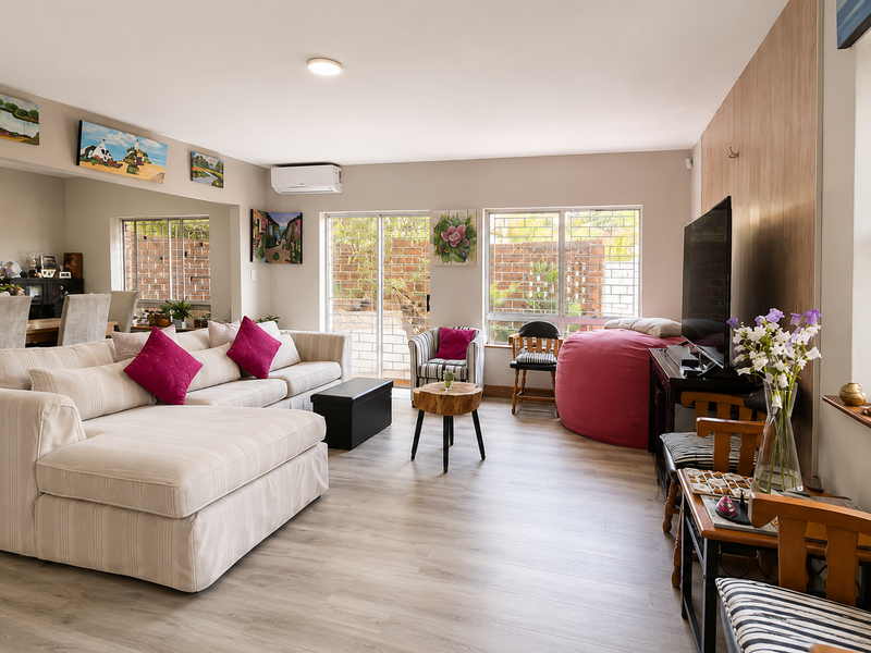 A bright and spacious living room featuring laminate flooring, split-system air conditioning, and large sliding glass doors providing access to the exterior.