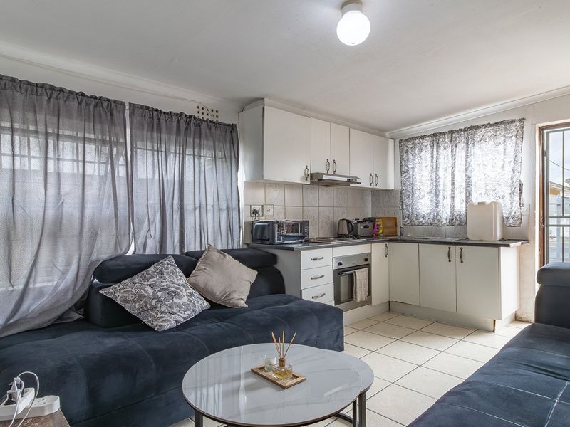 Open-plan living area featuring a compact kitchen with built-in cabinetry, oven, and extractor fan, finished with tiled flooring and direct exterior access.