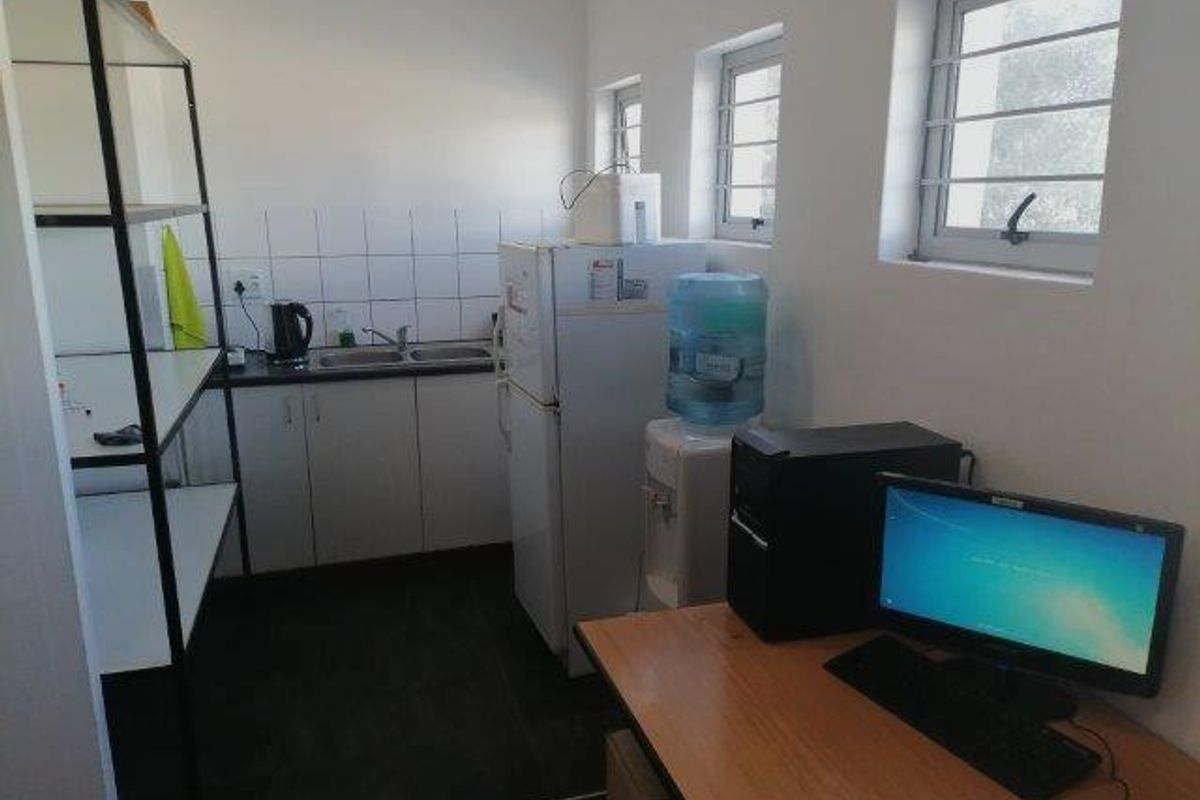 A functional office kitchenette area featuring built-in cabinetry, a stainless steel sink, and tiled splashbacks, integrated within a workspace environment.
