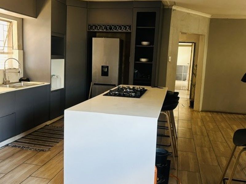 Modern kitchen featuring a central island with a gas hob, dark cabinetry, and wood-look tiled flooring, currently undergoing finishing touches.