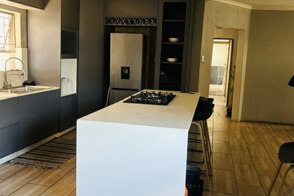 Modern kitchen featuring a central island with a gas hob, dark cabinetry, and wood-look tiled flooring, currently undergoing finishing touches.