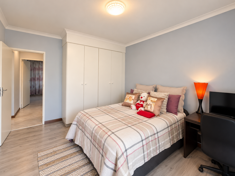 A well-maintained bedroom featuring light-toned laminate flooring, built-in wardrobes, and decorative cove cornicing, offering a clean and functional living space.